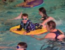 Boy on mat in swimming pool surrounded by swimmers